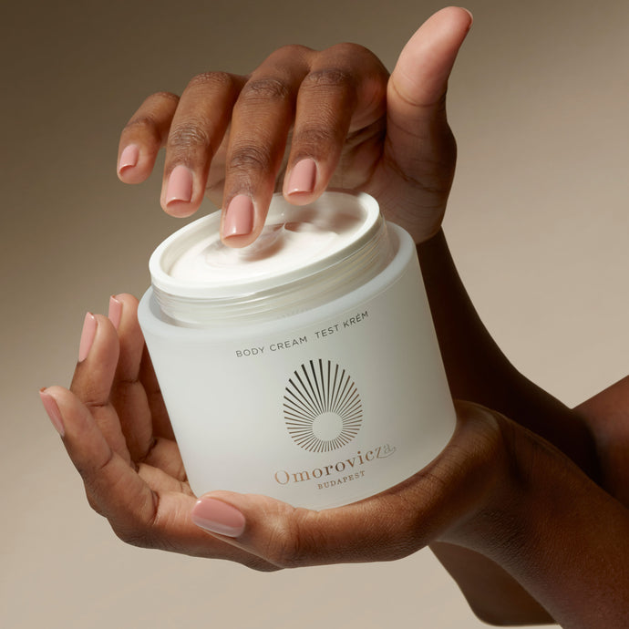 Hands are holding a jar of Omorovicza Body cream.