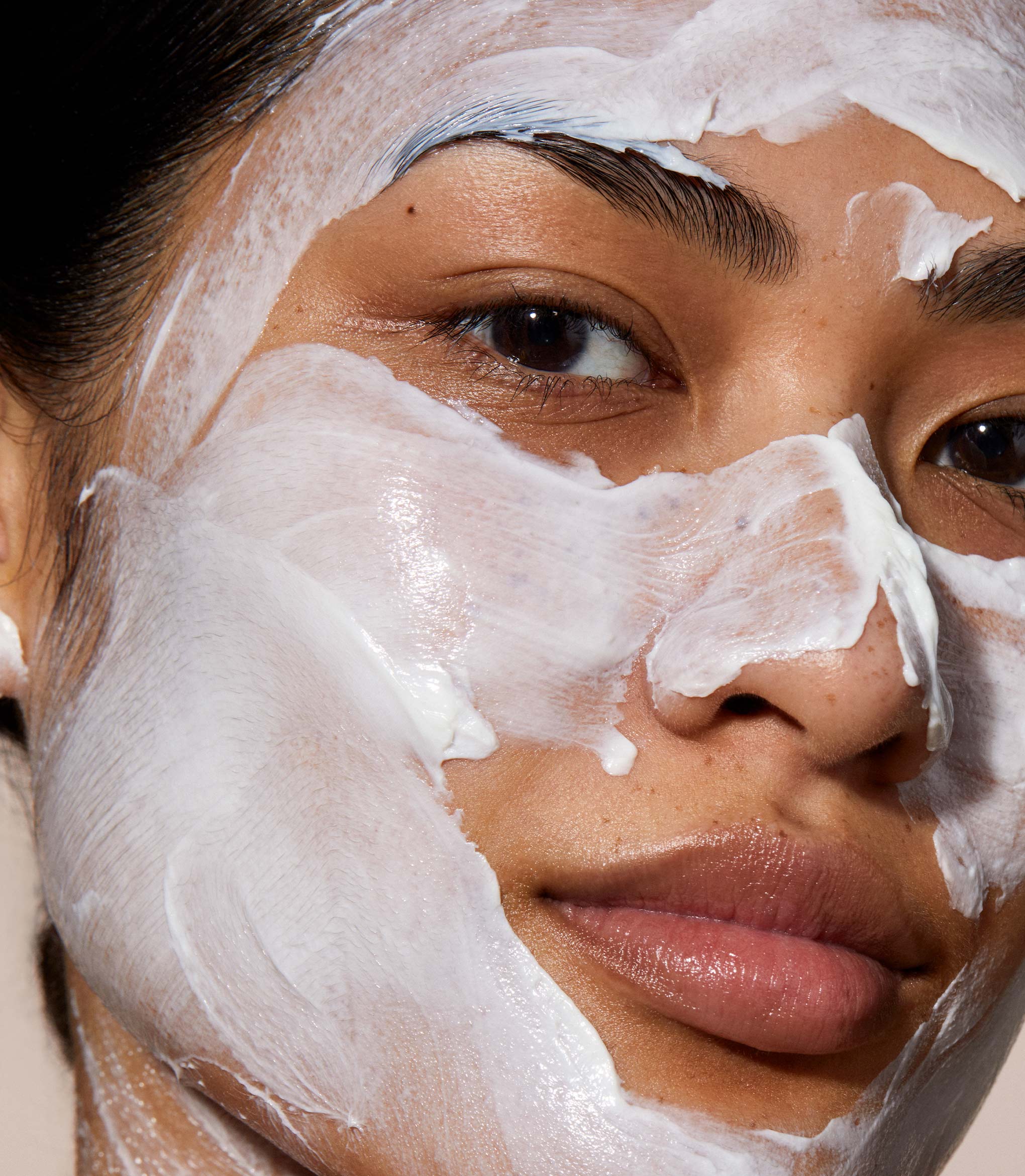 A close up of model's face with Queen cleanser applied over her face. the product is white and creamy applied in a thick layer.